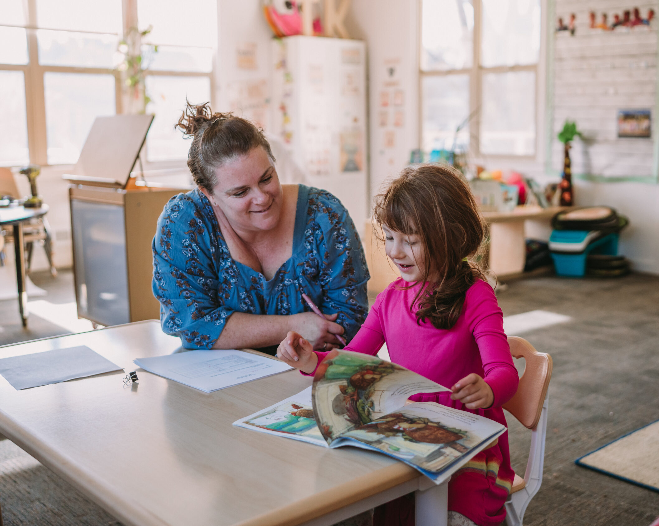 A TK student fliping through a book while her TK teacher proudly observes.