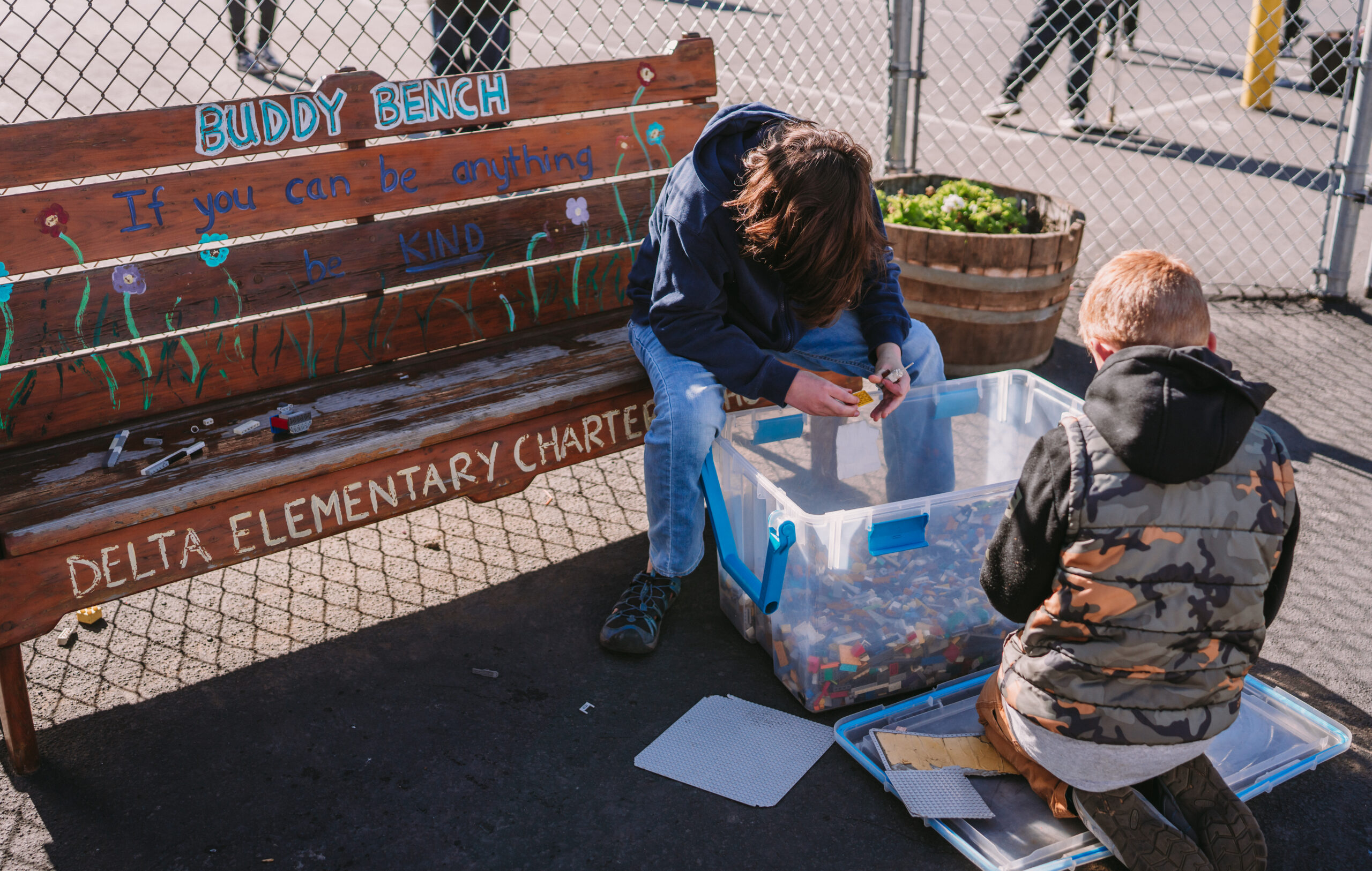 Two boys sitting on the buddy bench and playing with the legos in the big bin.