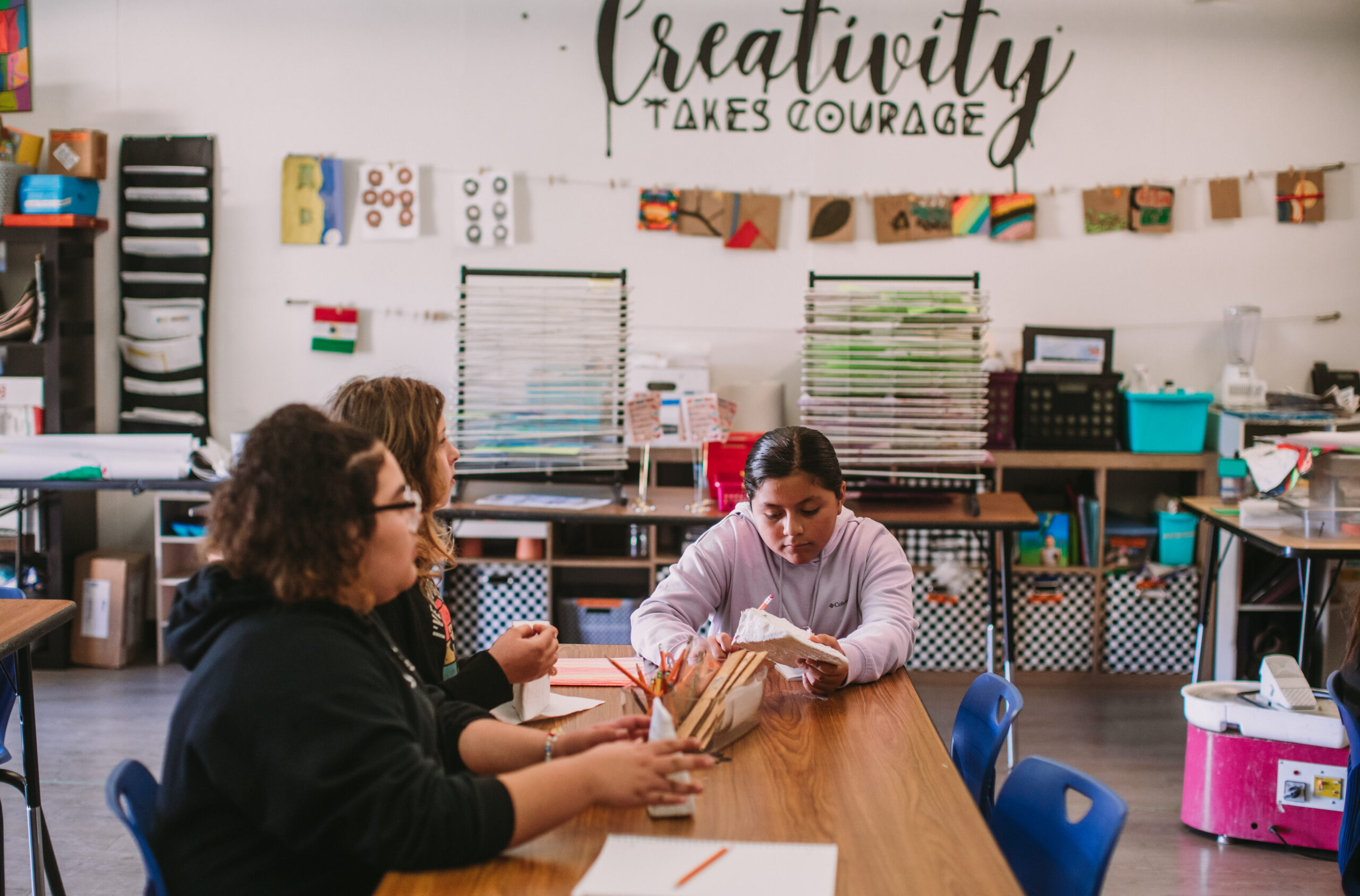 Three students sitting in the are classoom waiting for supplies and instructions.