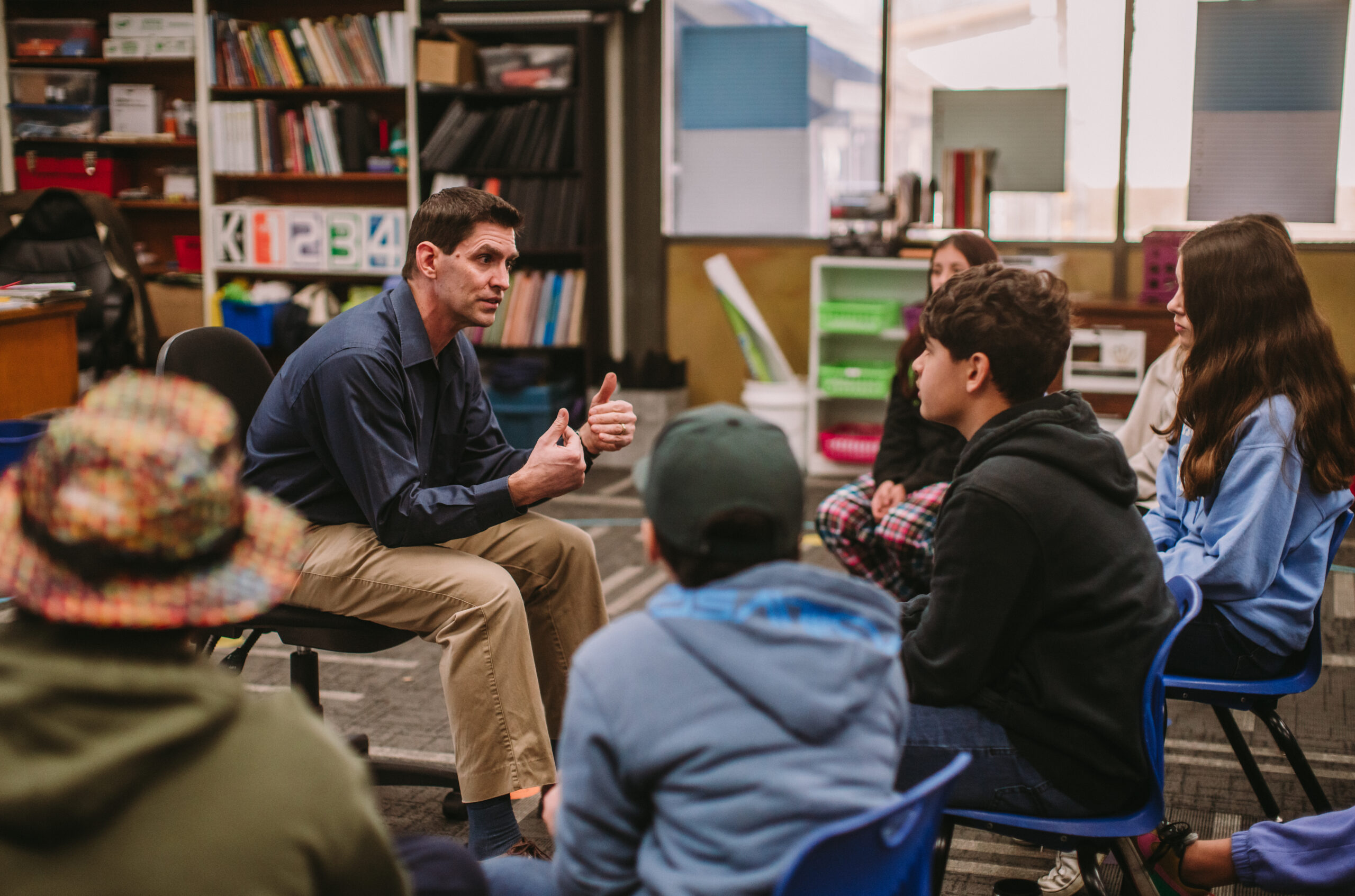 A group of sixth grade drama students sitting in chairs facing their teacher and activly listening.